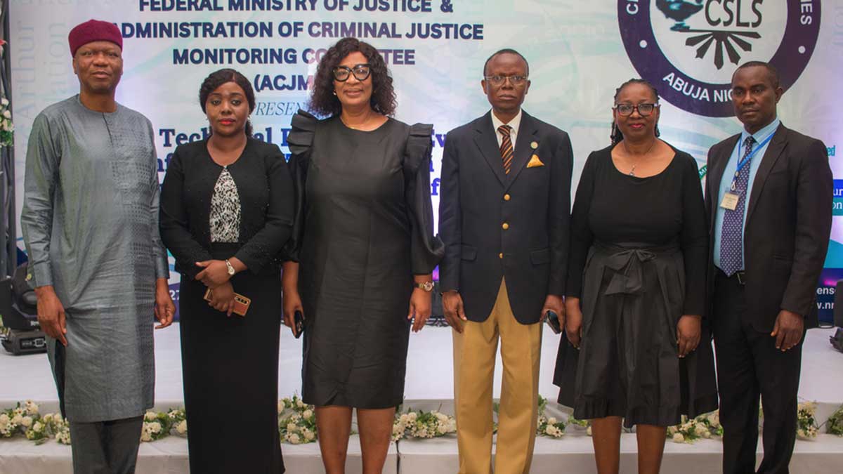 A group of six people in formal attire stands in front of a backdrop with a logo and text at an indoor event.